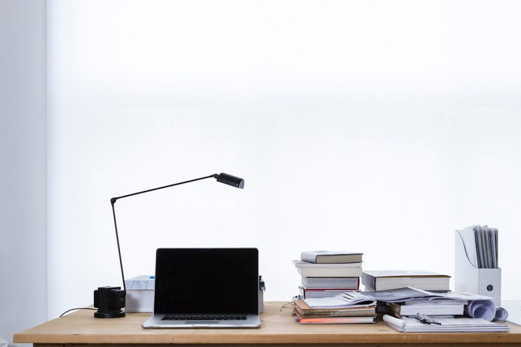 Laptop and a pile of books and file on a table with light.